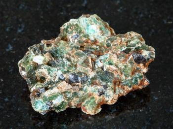 macro shooting of natural mineral - green beryl and emerald crystals in rough rock on black granite from Ural Mountains