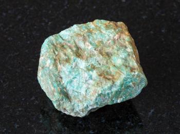macro shooting of natural mineral - rough Amazonite stone on black granite from Ural Mountains