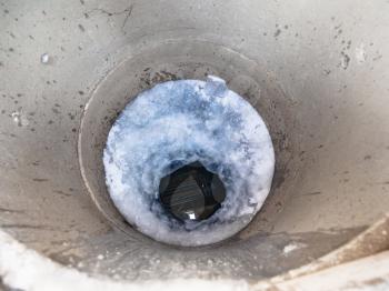 top view of frozen water and ice hole in concrete well in cold winter day