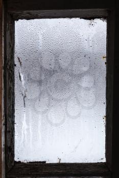 water from melting ice on surface of misted window in old rural house in winter