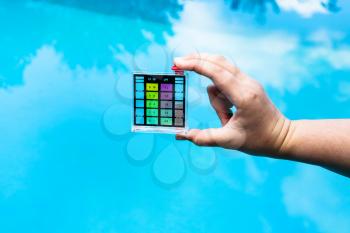 hand holds pH indicator for measure the acidity of water in a swimming pool