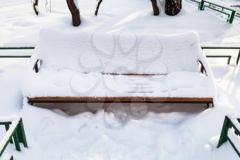 snow-covered bench at urban square in Moscow city in winter morning