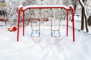 snow-covered public kids swing at residential district in Moscow city in winter morning