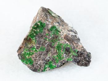 macro shooting of natural mineral - green Uvarovite crystals on rough Chromite stone on white marble from Ural Mountains