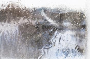 unfocused view of rural house through frozen window in overcast winter day (focus on the ice surface on the glass)