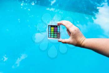 hand holds pH meter for measure the acidity of water in a swimming pool