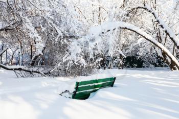 snow-covered bench in snowy urban garden in Moscow city in sunny winter morning