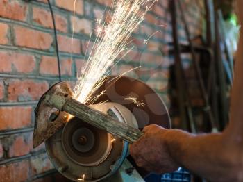 farmer sharpens garden tool on electric grindstone in rural shed