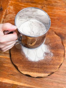 cooking of pie - sifting the flour through sifter on wooden board