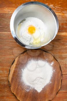 cooking of pie - pile of flour on board and flour with broken egg in steel bowl