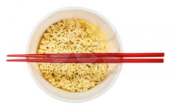 red chopsticks over open cup with dried instant noodles isolated on white background