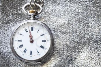 two minutes to twelve o'clock on vintage pocket watch on silver fabric background