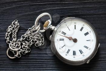 two minutes to twelve o'clock on old pocket watch with chain on black wooden background