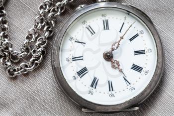 shabby silver pocket watch on gray textile background close up