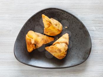 Indian cuisine - vegetable Samosa fried flaky pastry from green peas and potatoes on black plate on wooden table