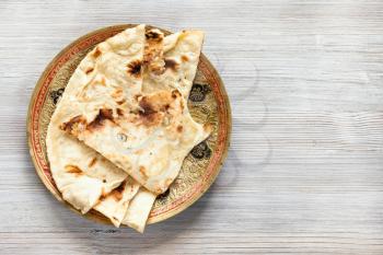 Indian cuisine - Naan flat bread baked in tandoor on brass plate on gray wood board