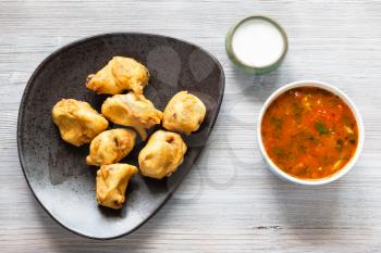 Indian cuisine - Chicken Pakoda pieces dipped in spiced butter on black plate served with sambar and chutney sauces on gray wooden board