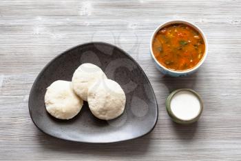 Indian cuisine - Idli Sambar steamed rice and urad bean dal dumplings served with sambar and chutney sauces on gray wooden board