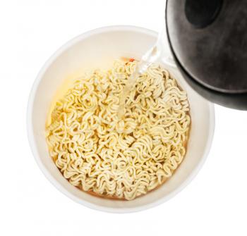 cooking instant noodles - pouring water from kettle into cup with dried instant noodles isolated on white background