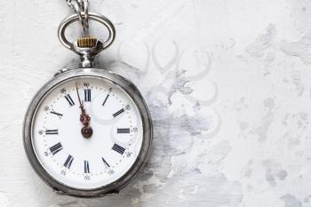 two minutes to twelve o'clock on vintage pocket watch on white concrete background