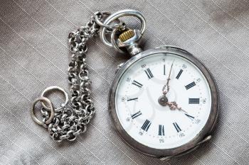 vintage silver pocket watch with chain on gray textile background