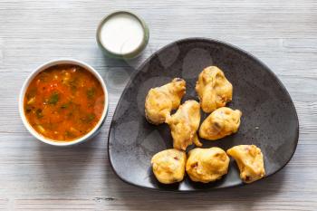 Indian cuisine - Chicken Pakoda pieces dipped in spiced butter on black plate served with sambar and chutney sauces on gray wooden table
