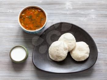 Indian cuisine - Idli Sambar steamed rice and urad bean dal dumplings served with sambar and chutney sauces on wooden table
