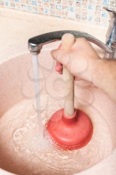 man clears kitchen sink drain by rubber plunger
