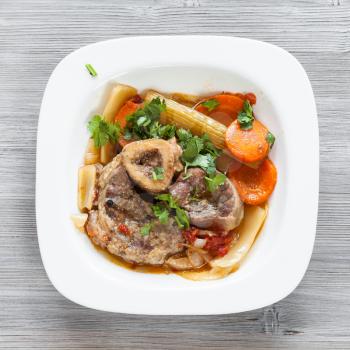 top view of italian dish Ossobuco in white plate on gray wooden board