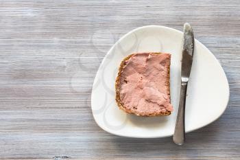 top view of bread sandwich with pate and steel knife on white plate on gray wooden board with blank copyspace