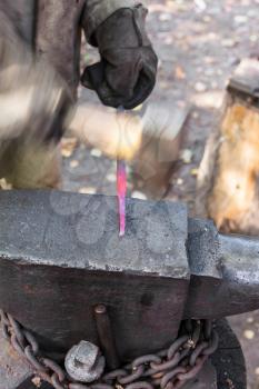 blacksmith forges steel bar to produce nail on outdoor anvil
