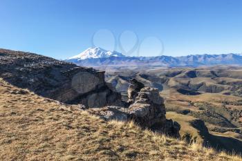 travel to North Caucasus region region - old rocks of Bermamyt Plateau and view of Mount Elbrus at morning