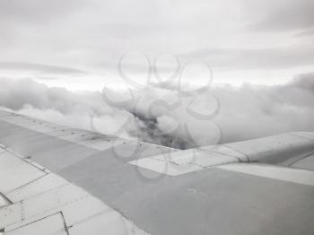 view of aircraft wing over gray clouds from the airplane porthole in flight in evening