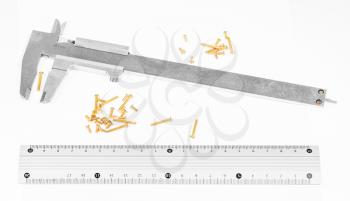 old steel calipers, metallic ruler and many of brass screws on white background