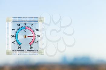 view of outdoor thermometer on home window and blurred skyline in hot evening