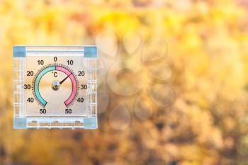 outdoor thermometer on home window and blurred yellow woods on background in sunny warm autumn day