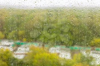 raindrops on glass of home window and blurred city garden on background on rainy autumn day