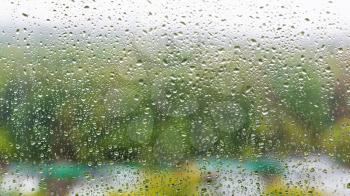 rain drops on surface of home window and blurred city park on background on rainy autumn day