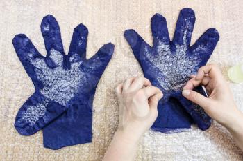 workshop of hand making a fleece gloves from blue Merino sheep wool using wet felting process - craftsman forms the finger of glove with the cutting pattern