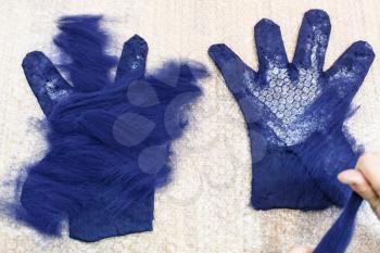 workshop of hand making a fleece gloves from blue Merino sheep wool using wet felting process - craftsman spreads second layer of fibers on glove