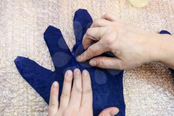 workshop of hand making a fleece gloves from blue Merino sheep wool using wet felting process - craftsman adds fibers on fingers of wet glove