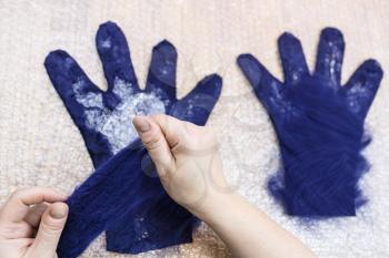 workshop of hand making a fleece gloves from blue Merino sheep wool using wet felting process- craftsman adds fibers of back side of glove on the cutting pattern