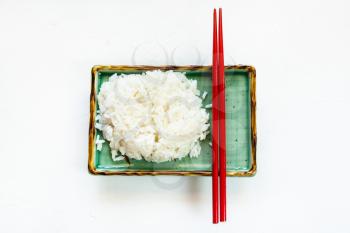 top view of boiled rice and red chopsticks on green plate on white concrete board with copyspace