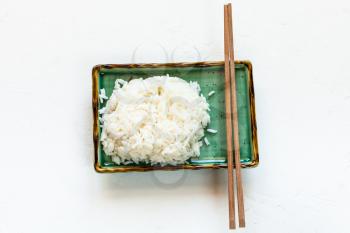 top view of portion of boiled rice and chopsticks on green plate on white concrete board with copyspace