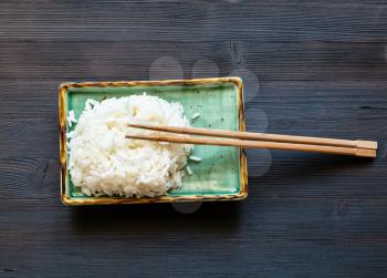 top view of boiled rice with chopsticks on green plate on dark brown table