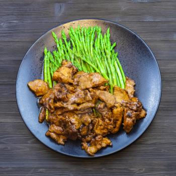 Chinese cuisine dish - above view of Beef fried in soy sauce with green asparagus on black plate on dark table