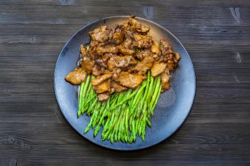 Chinese cuisine dish - top view of Beef fried in soy sauce with green asparagus on black plate on dark wooden board