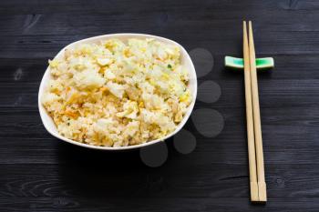 Chinese cuisine dish - served portion of Fried Rice with Shrimps, Vegetables and Eggs (Yangzhou rice) with chopsticks on dark wooden table