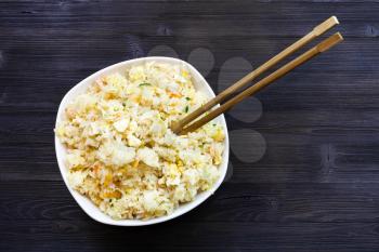 Chinese cuisine dish - top view of bowl with Fried Rice with Shrimps, Vegetables and Eggs (Yangzhou rice) with chopsticks on dark wooden table