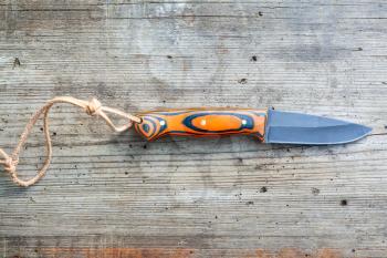 hand forged blackened steel knife with homemade epoxy and orange fabric handle with leather strap on old wooden board